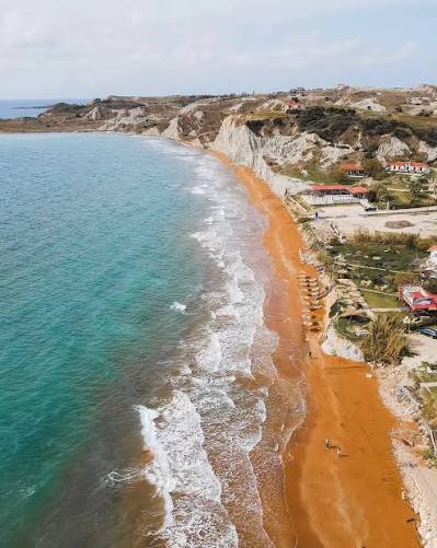 Η κοκκινωπή άμμος και η ακτογραμμή της παραλίας Ξι